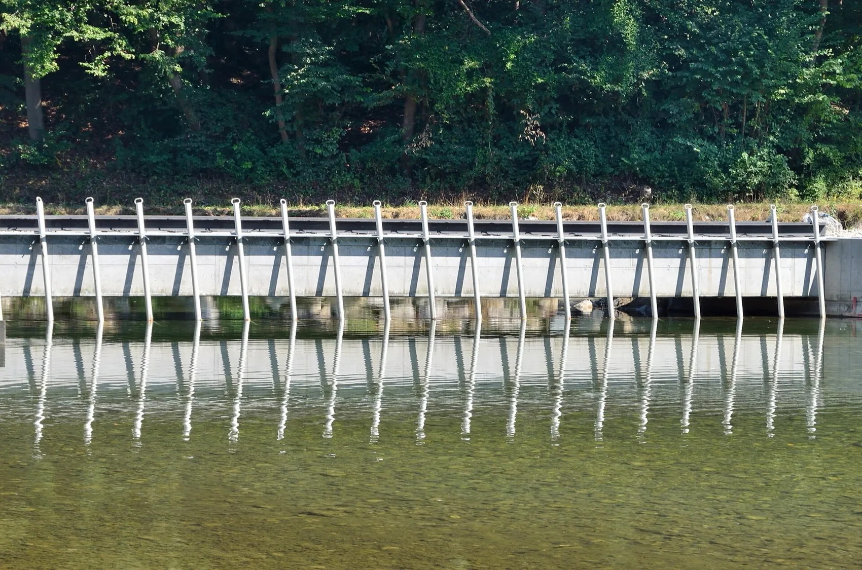 A rake bar screen across the intake of a run-of-river plant, reflected in still water